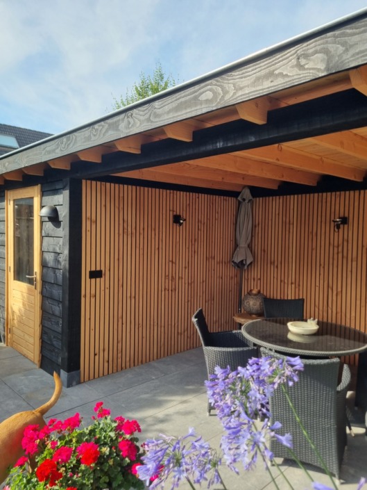 Lange houten overkapping op maat met aangebouwde berging en terrasmeubilair